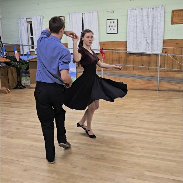 A dancer in a blue shirt spins his partner in a black dress at Let Freedom Swing